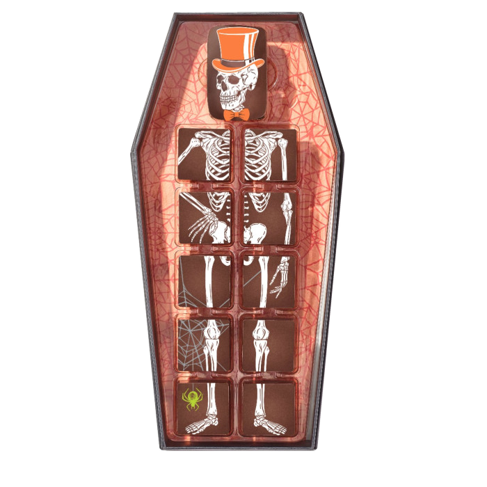 Top-down view of eleven Christopher Elbow chocolates forming a skeleton with an orange hat in an open coffin-shaped box