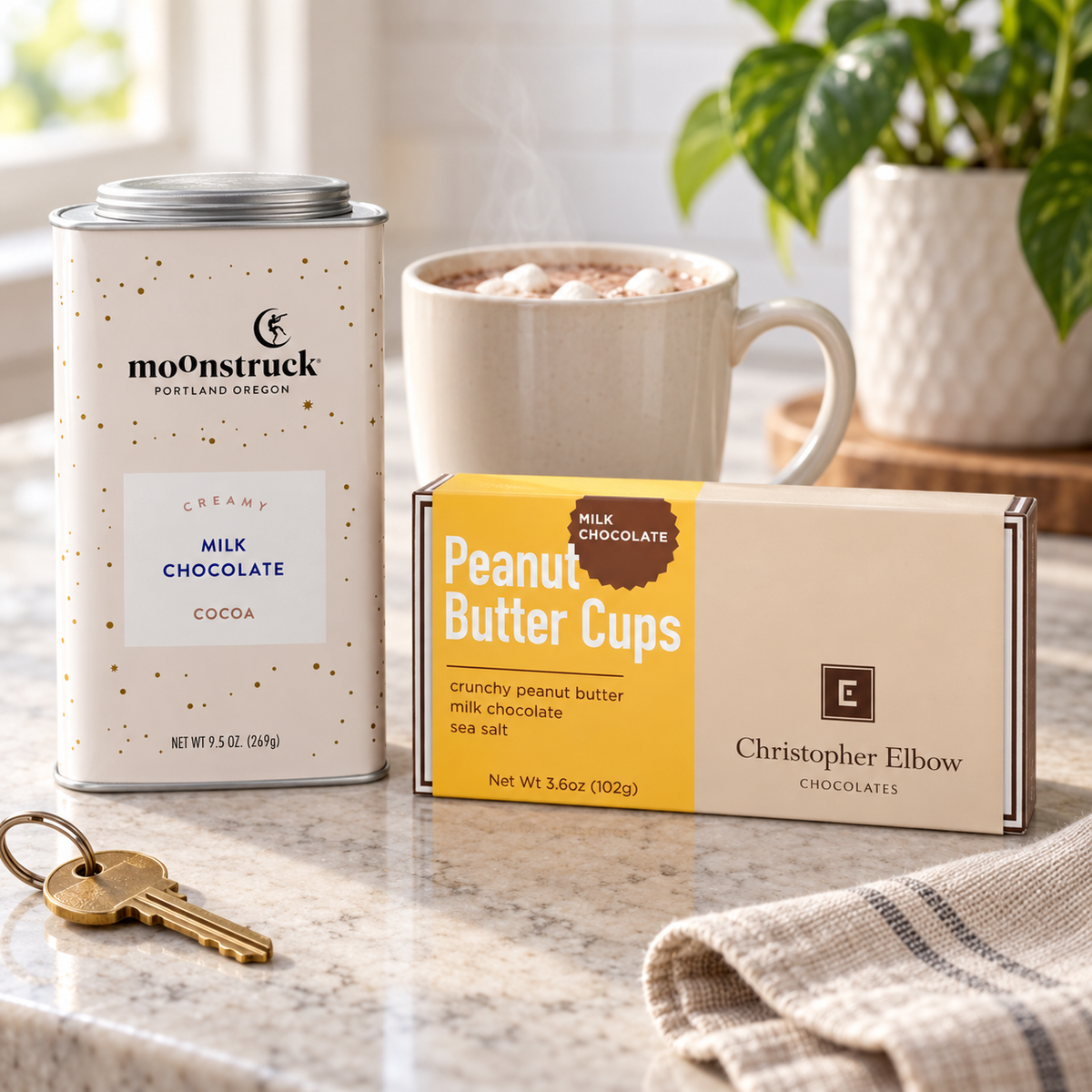 Moonstruck creamy milk hot cocoa tin and Christopher Elbow peanut butter cups box in a welcoming new-home kitchen